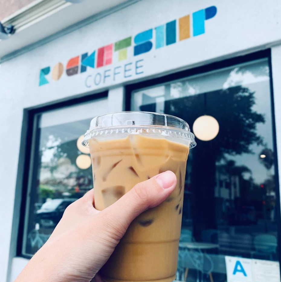 a person holding a cup of iced coffee infront of rocketship coffee